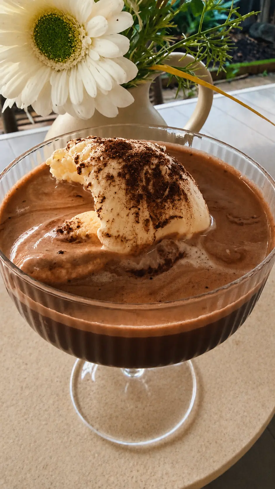Affogato served in a glass dish with a flower in the background